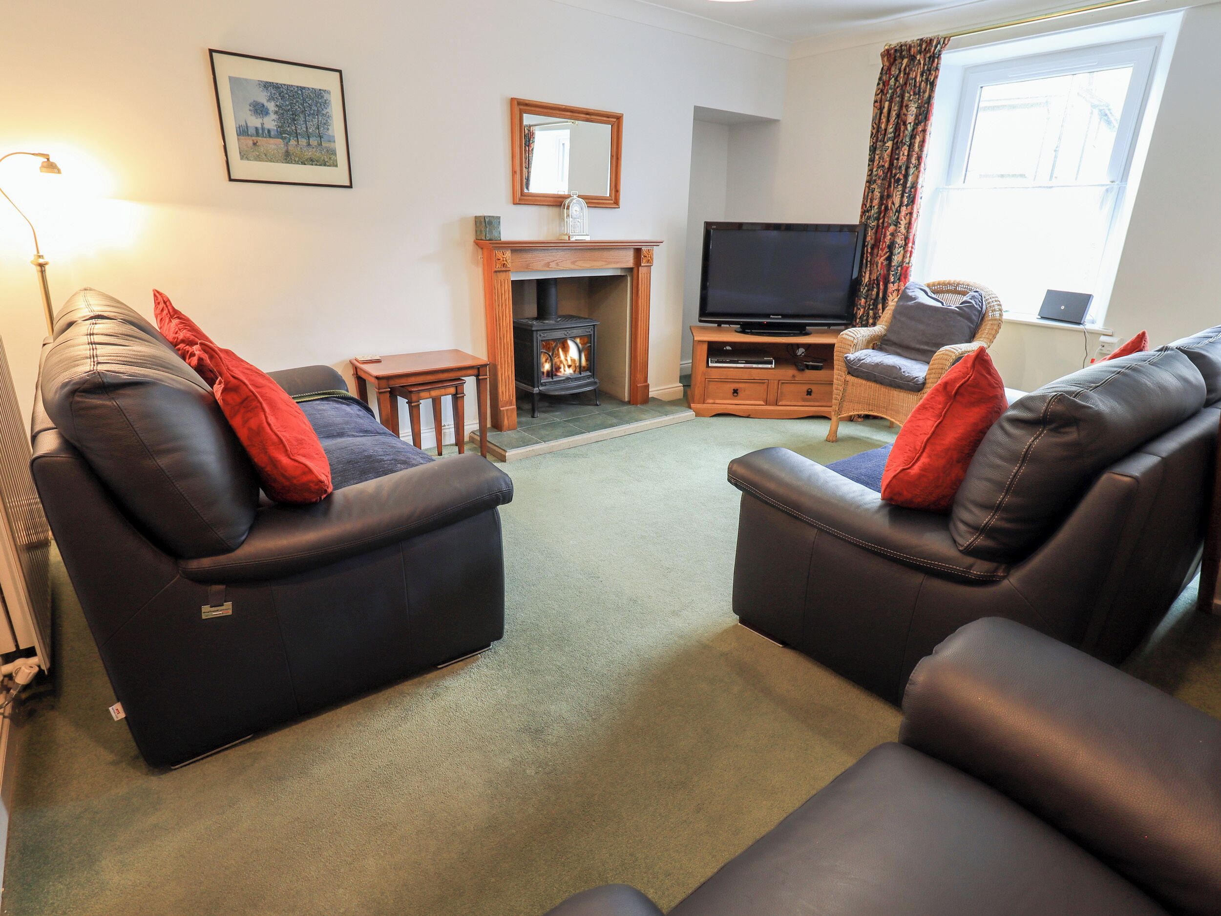 A cozy living room with two leather sofas, a fireplace, a television, and a window with curtains.