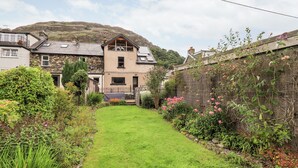 Ein Wohnhaus mit gepflegtem Rasen, ein Steinhaus mit Satteldach und ein Garten mit verschiedenen Pflanzen und Blumen.