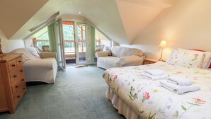 Ein gemütliches Schlafzimmer im Dachgeschoss mit einem Bett, zwei Stühlen, einer Kommode und einer Schiebetür zu einem Balkon.