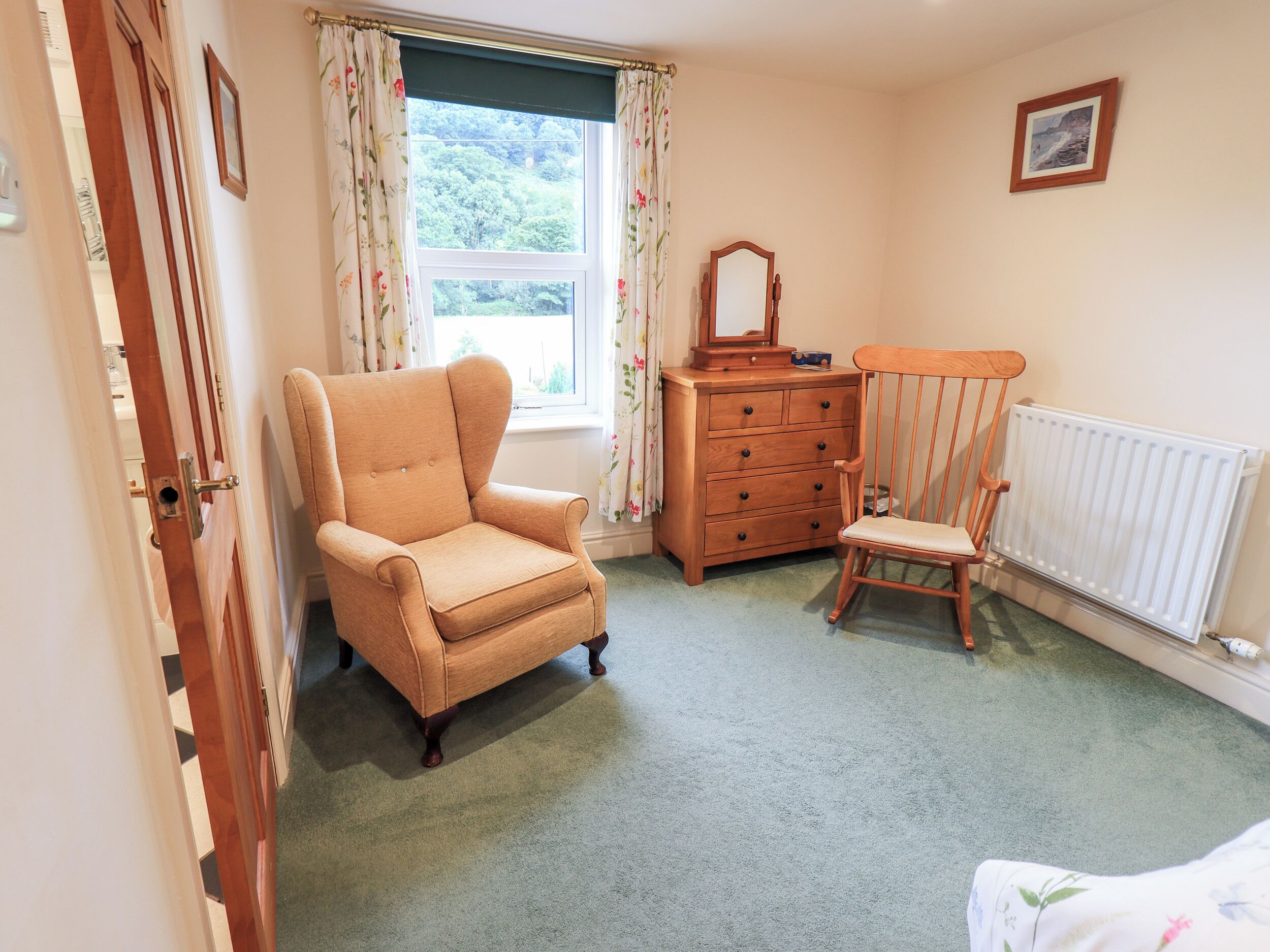 Une chambre avec une chaise en bois, une commode, un miroir et un radiateur.