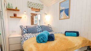 A cozy bedroom with a bed, patterned pillows, a yellow blanket, and a framed picture on the wall. - Langdale Lodge (Okehampton)