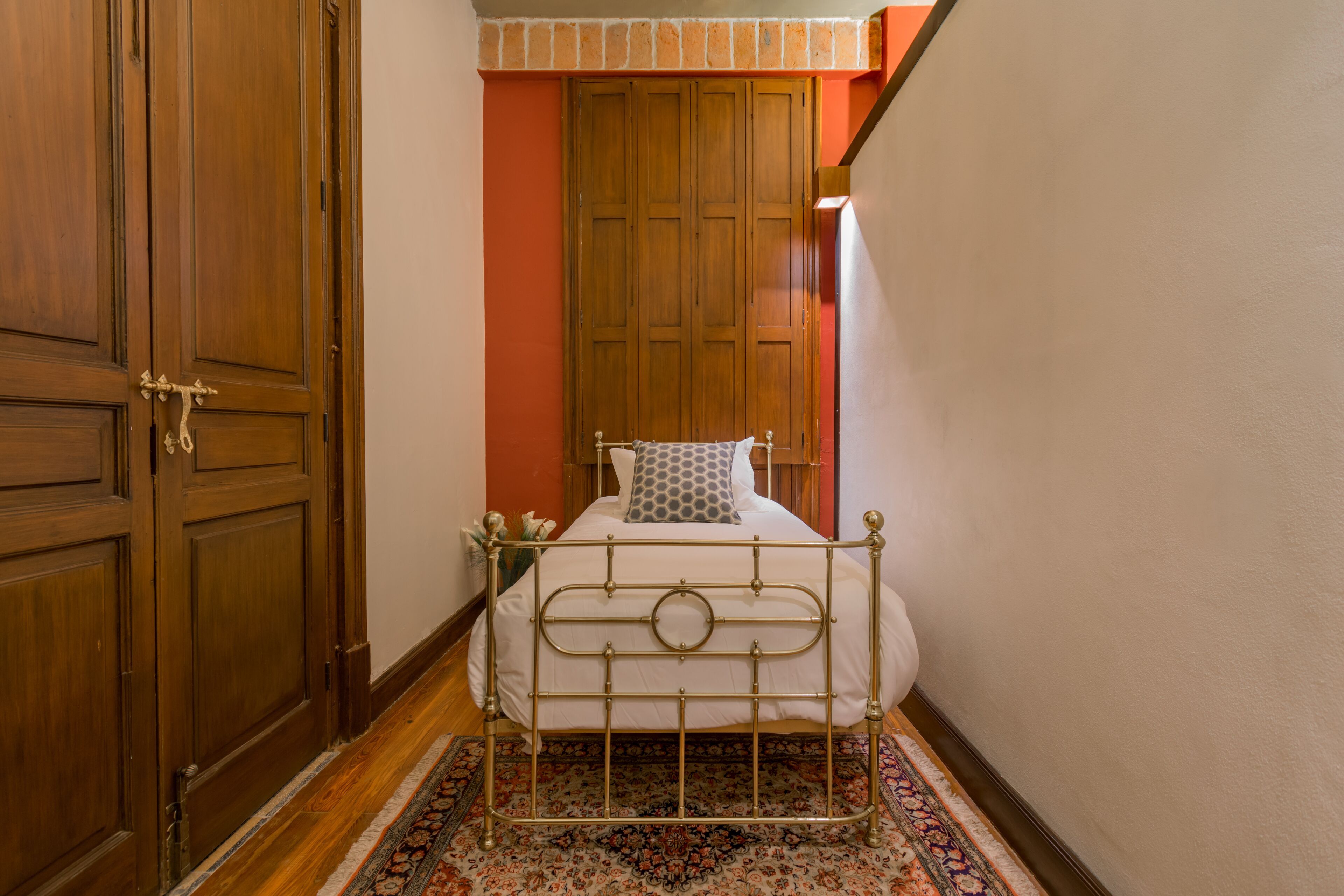 A narrow room with a bed, wooden wardrobe, and a patterned rug.