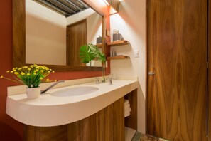 A bathroom with a wooden vanity, a white sink, a mirror, and a potted plant with yellow flowers.
