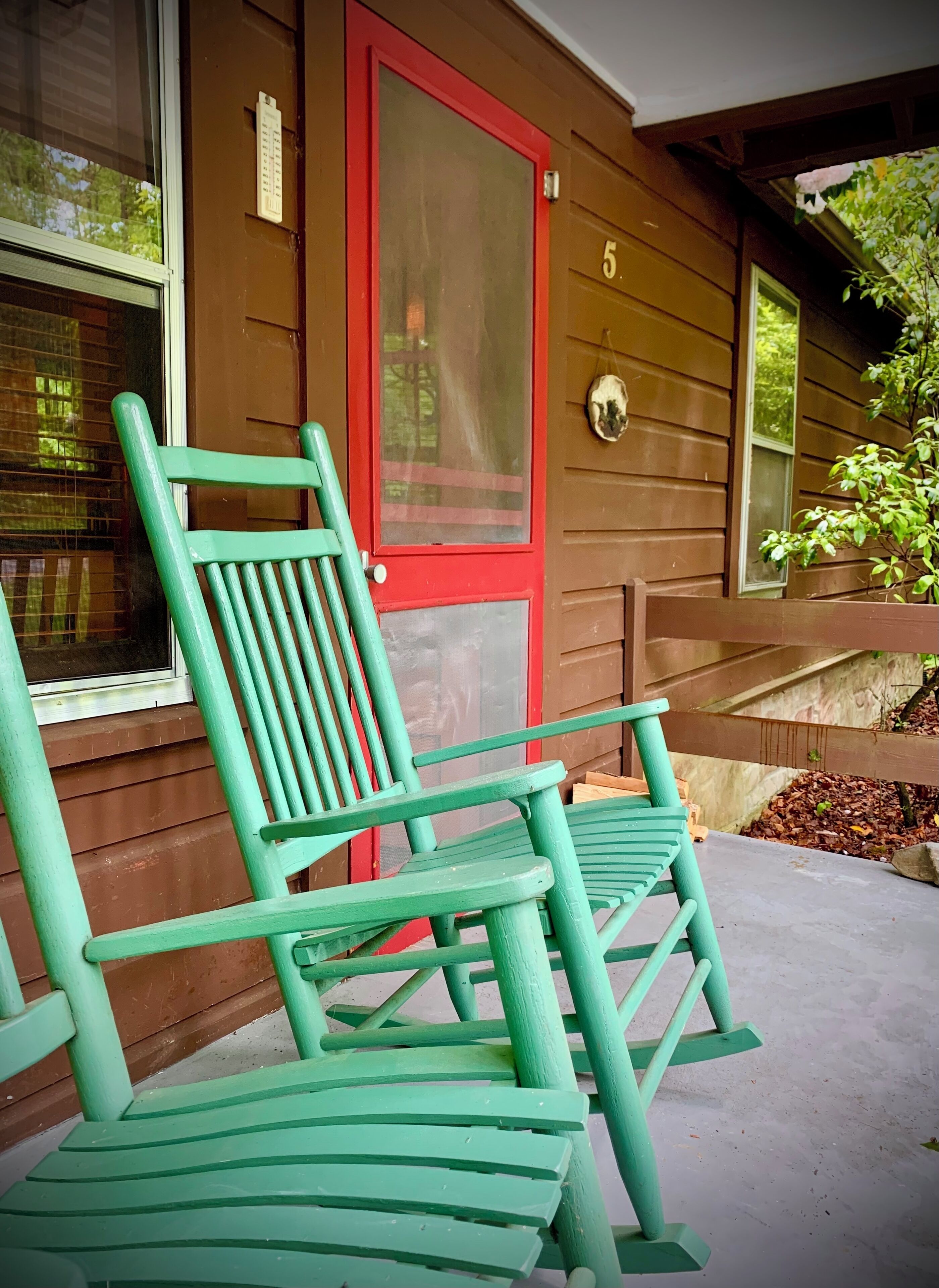 A porch with two green chairs and a red door with the number 5.