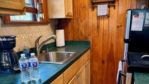 Une cuisine compacte avec des meubles en bois, un évier en acier inoxydable, une machine à café et deux bouteilles d’eau posées sur le comptoir.