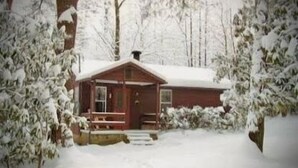 Une cabane dont le toit est recouvert de neige, entourée d’arbres.