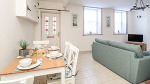 A modern living room with a green sofa, a dining table set with plates and glasses, and a TV on a wooden stand. - Bliss On The Bay (Weymouth)