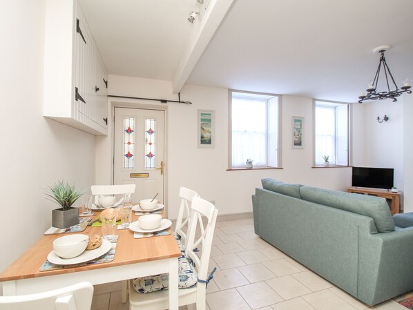 A modern living room with a green sofa, a dining table set with plates and glasses, and a TV on a wooden stand. - Bliss On The Bay (Weymouth)