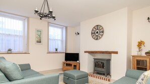 A living room with two grey sofas, a television on a wooden stand, a fireplace, and a clock on the wall. - Bliss On The Bay (Weymouth)