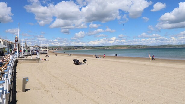A beach with a clear sky, a few people, and a clock tower in the background. - Bliss On The Bay (Weymouth)
