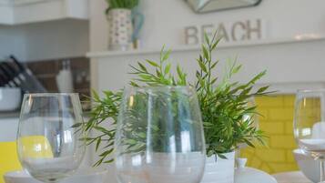 A dining table with a glass vase containing green foliage, a wine glass, and a bowl.