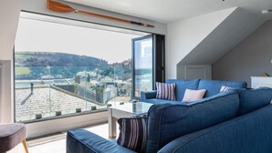 A modern living room with a large window offering a view of a cityscape and hills. - 2 Church Hill House (Salcombe)