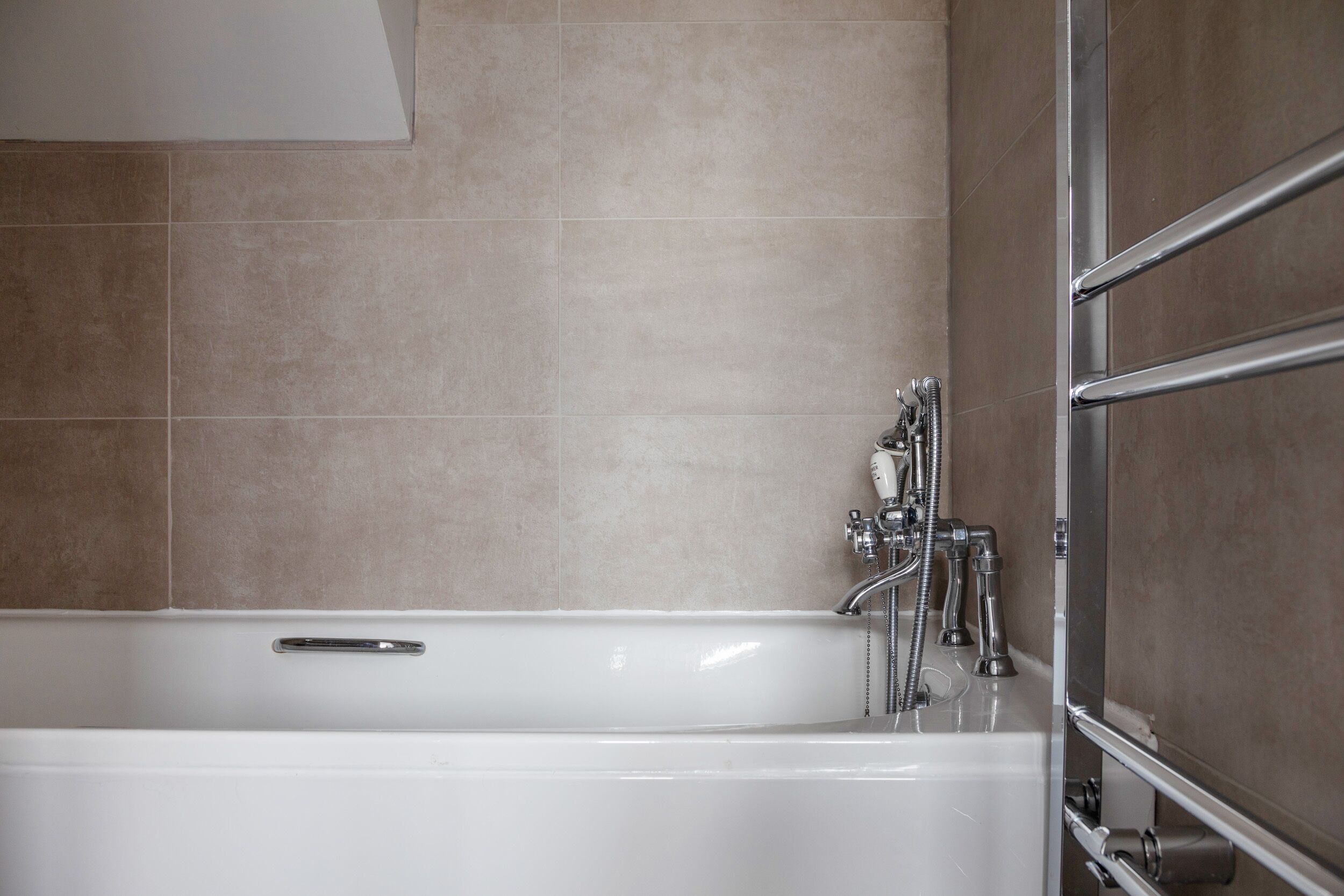 A modern bathroom with a bathtub, chrome fixtures, and beige tiles.