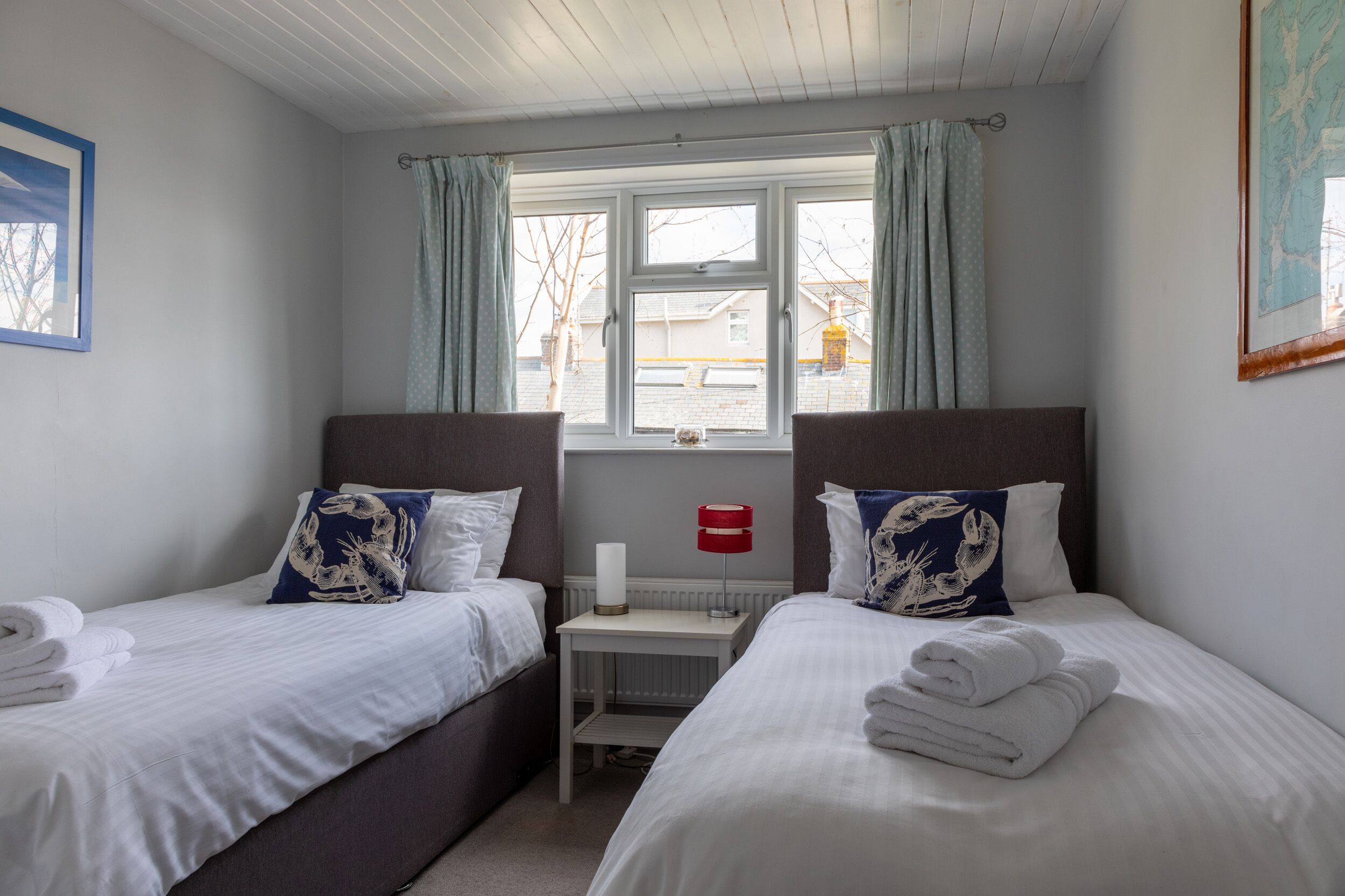 A hotel room with two beds, a small table with a lamp, and a window with curtains.