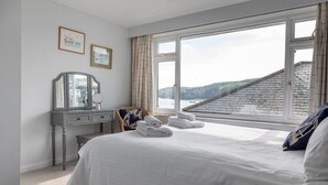 A bedroom with a large bed, a dresser, a chair, and a view of a building through a window. - 2 Church Hill House (Salcombe)