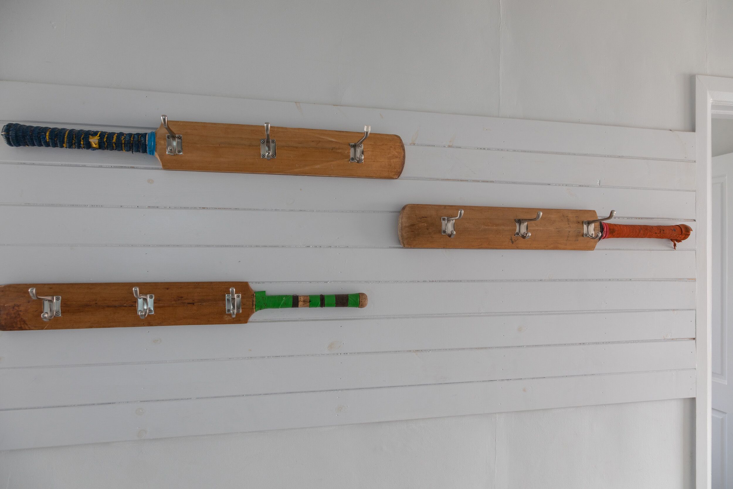 Four wooden bat hooks mounted on a white wall.