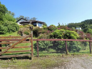 A rural property with a wooden gate, a house with a sloped roof, and a lush green landscape.