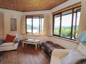 A cozy room with wooden flooring, a white sofa, a small table, and a view of a lake through large windows.