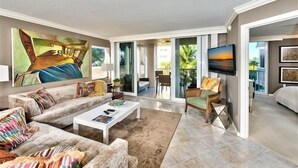 A spacious living room with a large painting, a sofa set, a coffee table, and a TV. - Steps to the beach w/ a beautiful pool view CL0101 (Naples)