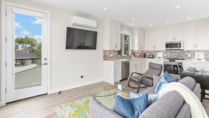 A modern kitchen with white cabinets, a large island, and a flat-screen TV mounted above it.