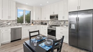 A modern kitchen with white cabinets, a stainless steel refrigerator, a microwave, and a stove.
