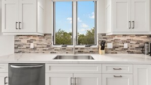 A modern kitchen with white cabinets, a double sink, and a stone backsplash.