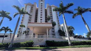 A high-rise hotel with a central entrance, palm trees, and a clear blue sky. - Superb Gulf views in a renovated unit - CL0302 (Naples)