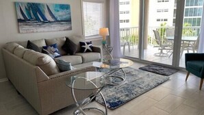 A modern living room with a sofa, a glass coffee table, and a view of a balcony. - Superb Gulf views in a renovated unit - CL0302 (Naples)