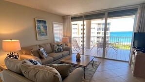 Un salon comprenant un canapé, une table basse et un téléviseur. Il y a un balcon avec vue sur l’océan.