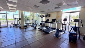 Une salle de sport équipée de divers appareils d’exercice, dotée de grandes fenêtres et d’un sol carrelé.