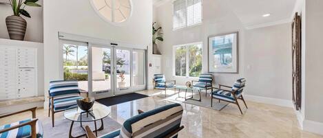 A spacious lobby with a high ceiling, large windows, and a seating area with striped chairs and a glass table.