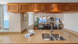 A kitchen with granite countertops, stainless steel sink, wooden cabinets, and a view to the living area. - Bright, airy Gulf of Mexico views! - WS1101 (Naples)