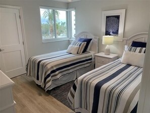 A bedroom with two beds, a window, a nightstand, and a framed picture on the wall. - Views of palm trees, sand and the Gulf! - WS0304 (Naples)