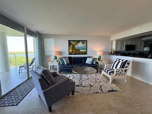 Una sala de estar moderna con un sofá, un sillón y una mesa de centro, un cuadro en la pared y vistas al exterior.