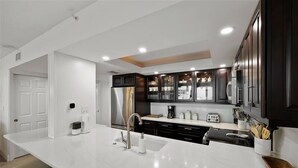 Una cucina moderna con ripiani bianchi, mobili scuri ed elettrodomestici in acciaio inossidabile.