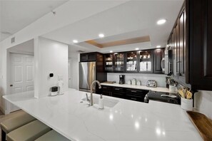 Una cocina moderna con encimeras blancas, armarios oscuros y electrodomésticos de acero inoxidable.