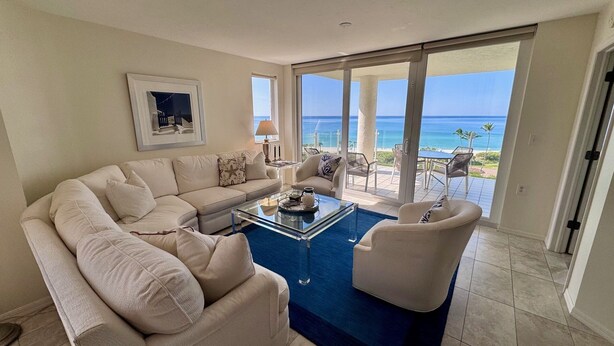 A living room with a beige sofa, a glass coffee table, and a view of the ocean through large sliding glass doors. - Bright corner views of the Gulf of Mexico! - WS0701 (Naples)