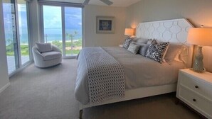 A bedroom with a large bed, a ceiling fan, a nightstand, a chair, and a view of the ocean. - Bright corner views of the Gulf of Mexico! - WS0701 (Naples)