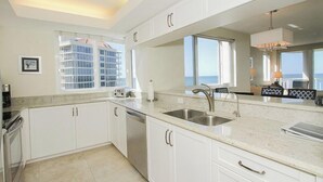 A modern kitchen with white cabinets, a stainless steel sink, and a view of the ocean through large windows. - Bright corner views of the Gulf of Mexico! - WS0701 (Naples)