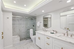 Een moderne badkamer met een douchecabine van glas, een wit toilet en een wastafel met gouden knoppen.