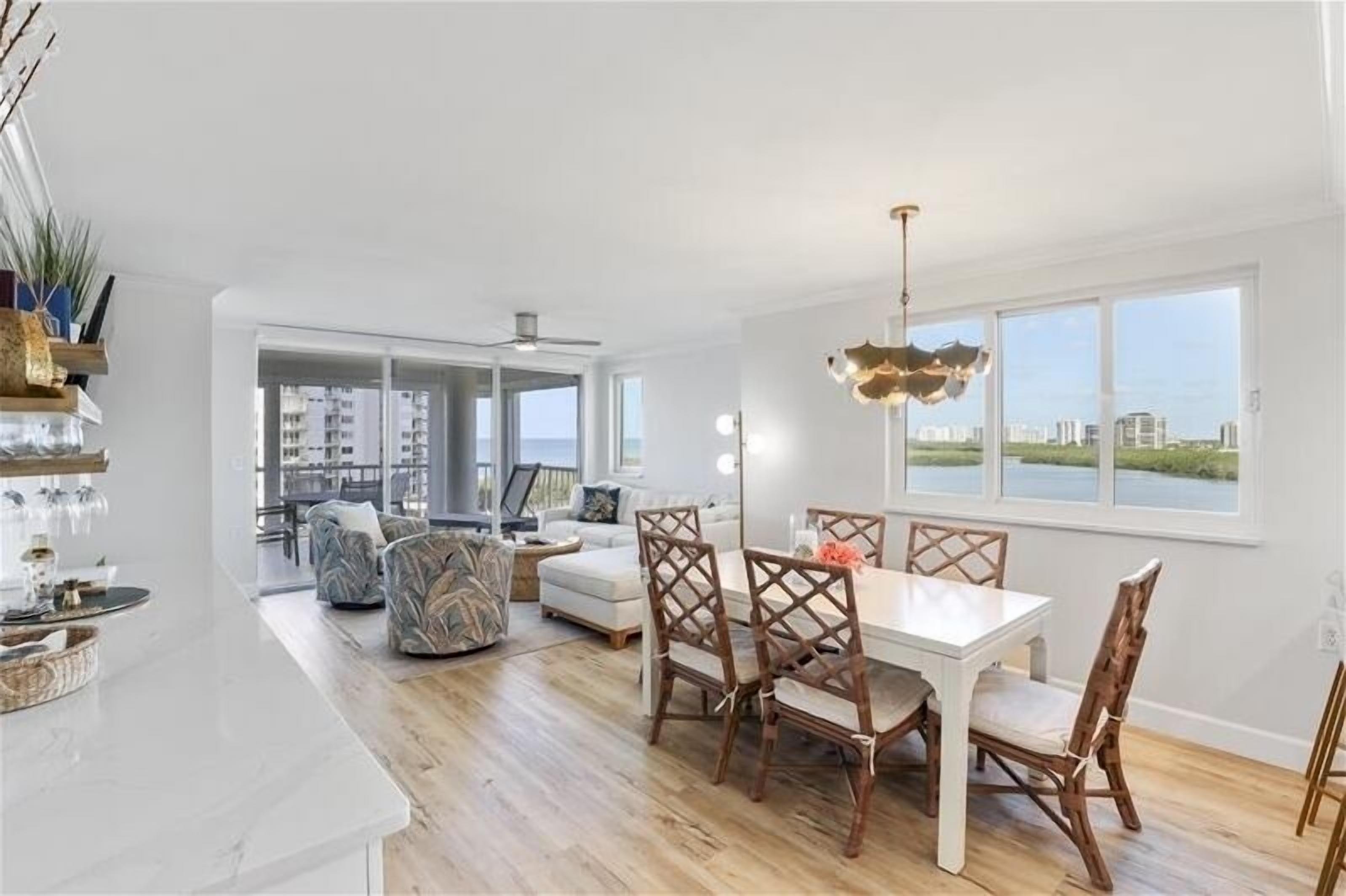 A spacious living area with a dining table and chairs, a sofa, and a view of the city through large windows.