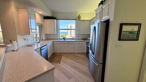 Una cocina moderna con armarios blancos, un refrigerador de acero inoxidable y una ventana con vistas a edificios.