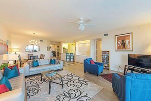 A spacious living room with a sofa, armchairs, a coffee table, and a TV. There is a ceiling fan, a bookshelf, and a painting on the wall. - 2 blocks from the beach with bay and gulf views - Reg 2-1004 (Naples)