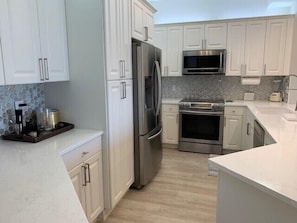 A modern kitchen with white cabinets, stainless steel appliances, a stone backsplash, and a wooden countertop. - 3 bedroom with spectacular bay and gulf views in the distance - Reg 2-905 (Naples)