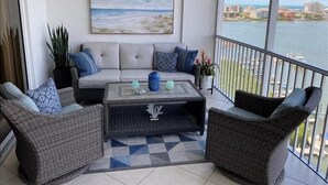 Ein Balkon mit einer Couch, zwei Korbstühlen, einem Couchtisch und einem Strandbild.