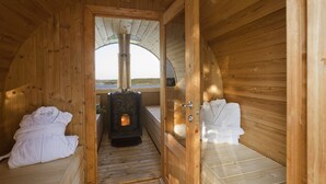 Et sauna-rum med træbænk, saunaovn og en glasdør til et udendørs område.