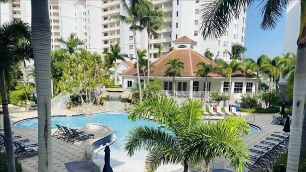 A resort pool area with lounge chairs, palm trees, and a building in the background. - Great location! 2 blocks from the beach with beautiful pool views -Reg 5-404 (Naples)