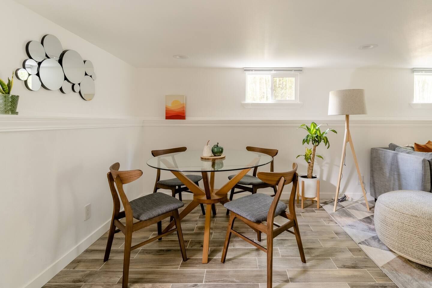 A dining area with a round glass table, wooden chairs, a potted plant, and a floor lamp.