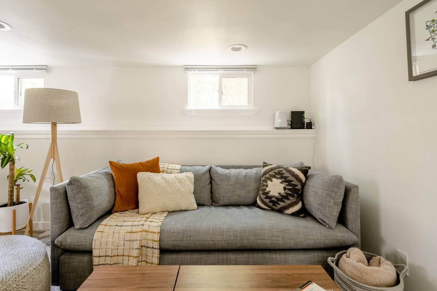 Ein Wohnzimmer mit grauem Sofa, einer Stehlampe, einem kleinen Tisch und einem Haustierbett.