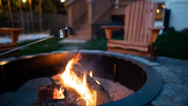 A fire pit with a marshmallow on a stick, surrounded by outdoor furniture and a building in the background. - Enjoy everything Seattle has to offer in centrally located Central District (Seattle)
